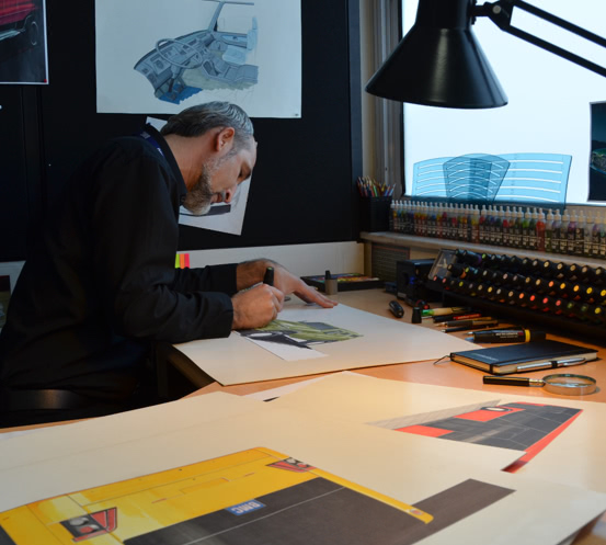 A man sitting at a desk with a computer on a table and drawing car design with pencil on paper 1